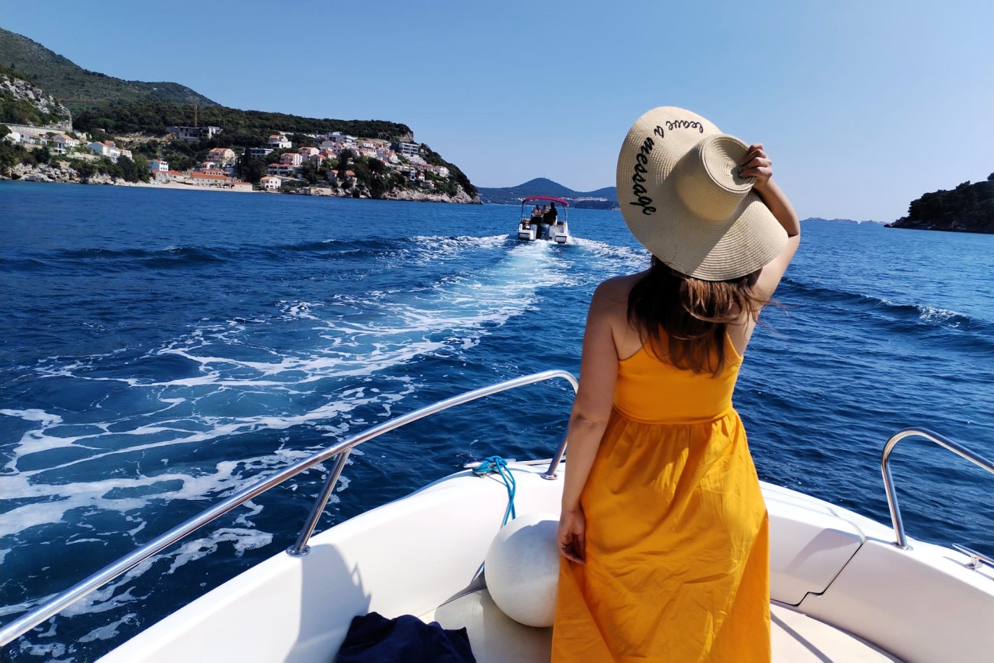 A girl with a hat on the bow of a boat with her back to the camera